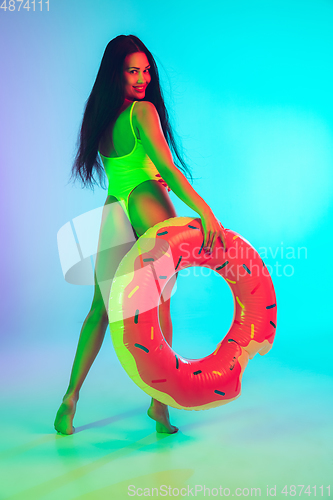 Image of Beautiful girl in fashionable swimsuit isolated on gradient studio background in neon light. Summer, resort, fashion and weekend concept