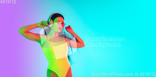 Image of Beautiful girl in fashionable swimsuit isolated on gradient studio background in neon light. Summer, resort, fashion and weekend concept. Flyer with copyspace.