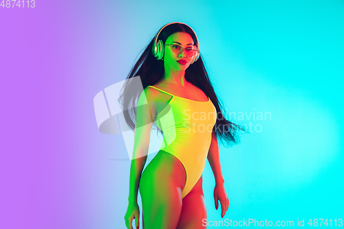 Image of Beautiful girl in fashionable swimsuit isolated on gradient studio background in neon light. Summer, resort, fashion and weekend concept