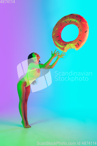 Image of Beautiful girl in fashionable swimsuit isolated on gradient studio background in neon light. Summer, resort, fashion and weekend concept