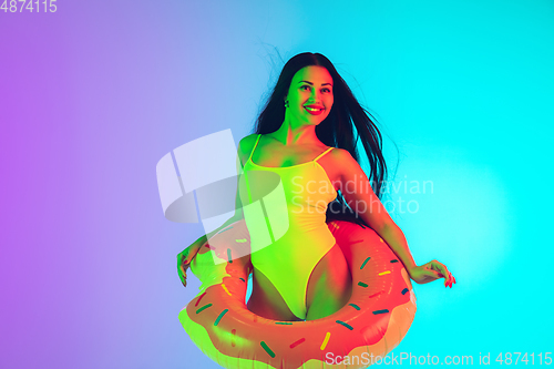 Image of Beautiful girl in fashionable swimsuit isolated on gradient studio background in neon light. Summer, resort, fashion and weekend concept