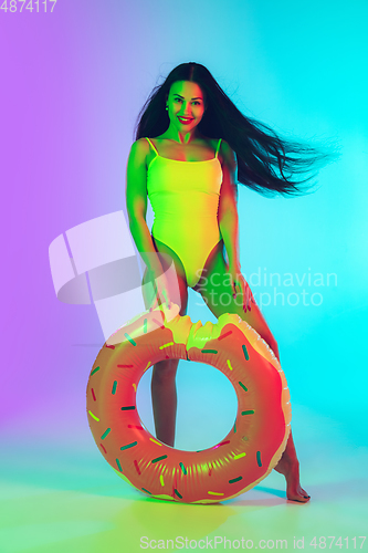 Image of Beautiful girl in fashionable swimsuit isolated on gradient studio background in neon light. Summer, resort, fashion and weekend concept