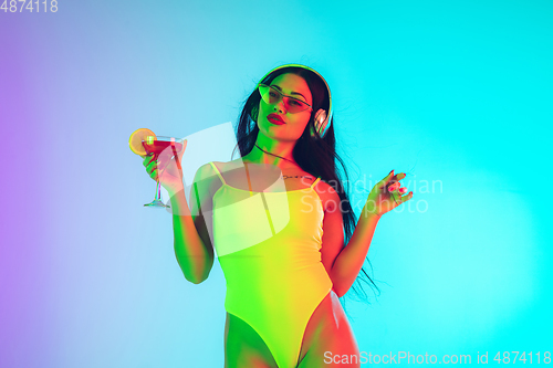 Image of Beautiful girl in fashionable swimsuit isolated on gradient studio background in neon light. Summer, resort, fashion and weekend concept