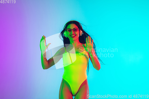 Image of Beautiful girl in fashionable swimsuit isolated on gradient studio background in neon light. Summer, resort, fashion and weekend concept