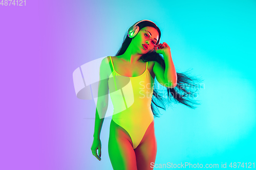 Image of Beautiful girl in fashionable swimsuit isolated on gradient studio background in neon light. Summer, resort, fashion and weekend concept