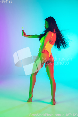 Image of Beautiful girl in fashionable swimsuit isolated on gradient studio background in neon light. Summer, resort, fashion and weekend concept