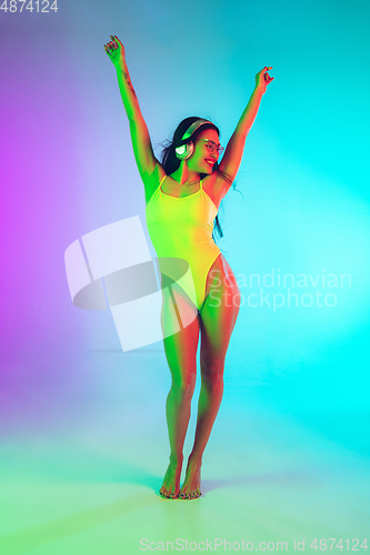 Image of Beautiful girl in fashionable swimsuit isolated on gradient studio background in neon light. Summer, resort, fashion and weekend concept