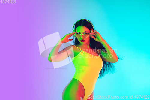 Image of Beautiful girl in fashionable swimsuit isolated on gradient studio background in neon light. Summer, resort, fashion and weekend concept