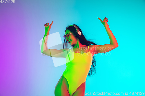 Image of Beautiful girl in fashionable swimsuit isolated on gradient studio background in neon light. Summer, resort, fashion and weekend concept