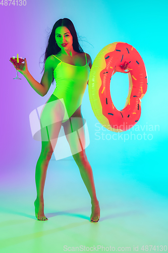 Image of Beautiful girl in fashionable swimsuit isolated on gradient studio background in neon light. Summer, resort, fashion and weekend concept