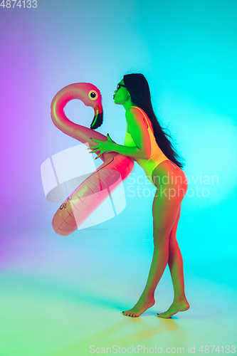 Image of Beautiful girl in fashionable swimsuit isolated on gradient studio background in neon light. Summer, resort, fashion and weekend concept