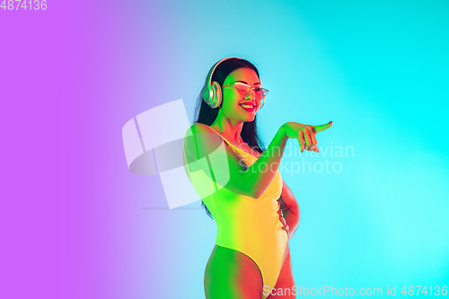 Image of Beautiful girl in fashionable swimsuit isolated on gradient studio background in neon light. Summer, resort, fashion and weekend concept