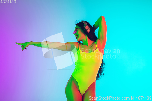 Image of Beautiful girl in fashionable swimsuit isolated on gradient studio background in neon light. Summer, resort, fashion and weekend concept