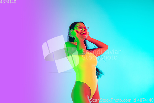 Image of Beautiful girl in fashionable swimsuit isolated on gradient studio background in neon light. Summer, resort, fashion and weekend concept