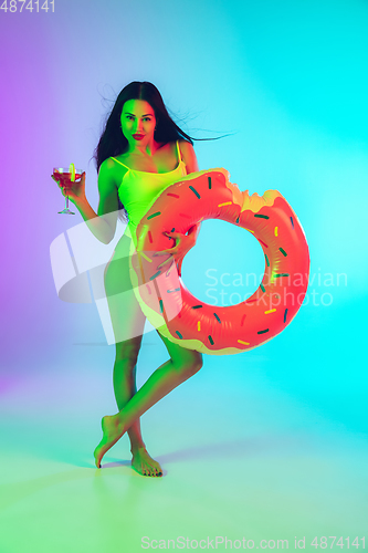 Image of Beautiful girl in fashionable swimsuit isolated on gradient studio background in neon light. Summer, resort, fashion and weekend concept