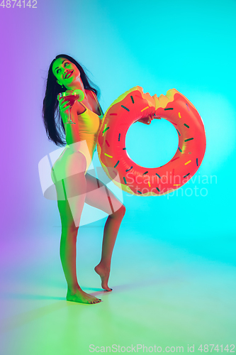 Image of Beautiful girl in fashionable swimsuit isolated on gradient studio background in neon light. Summer, resort, fashion and weekend concept