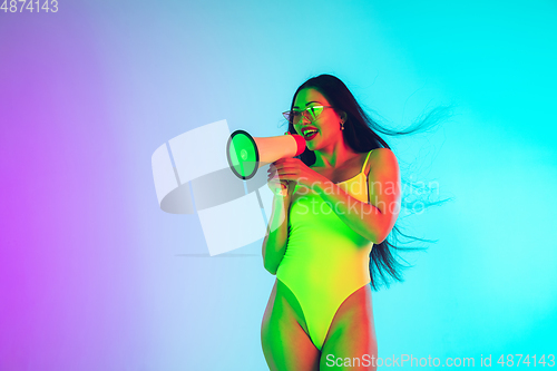 Image of Beautiful girl in fashionable swimsuit isolated on gradient studio background in neon light. Summer, resort, fashion and weekend concept