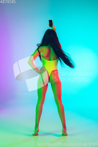 Image of Beautiful girl in fashionable swimsuit isolated on gradient studio background in neon light. Summer, resort, fashion and weekend concept