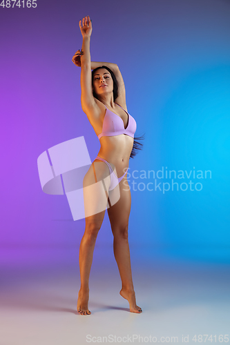 Image of Fashion portrait of young fit and sportive woman in stylish purple luxury swimwear on gradient background. Perfect body ready for summertime.