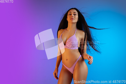 Image of Fashion portrait of young fit and sportive woman in stylish purple luxury swimwear on gradient background. Perfect body ready for summertime.