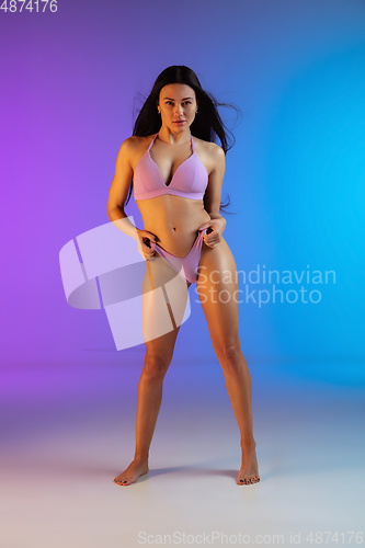 Image of Fashion portrait of young fit and sportive woman in stylish purple luxury swimwear on gradient background. Perfect body ready for summertime.