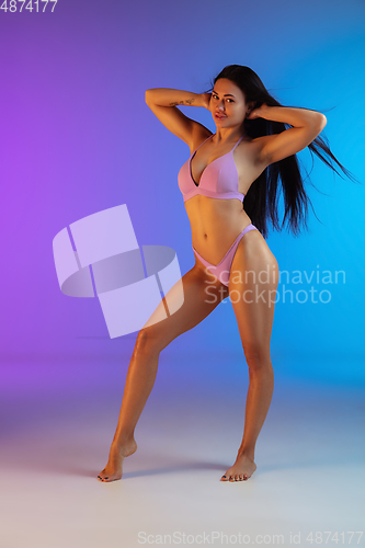 Image of Fashion portrait of young fit and sportive woman in stylish purple luxury swimwear on gradient background. Perfect body ready for summertime.