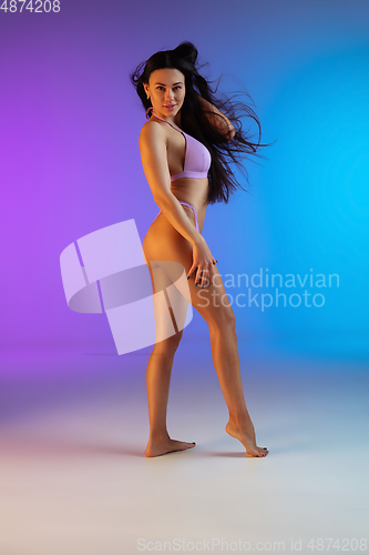 Image of Fashion portrait of young fit and sportive woman in stylish purple luxury swimwear on gradient background. Perfect body ready for summertime.