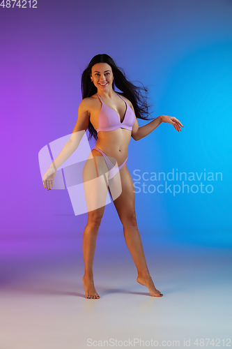 Image of Fashion portrait of young fit and sportive woman in stylish purple luxury swimwear on gradient background. Perfect body ready for summertime.