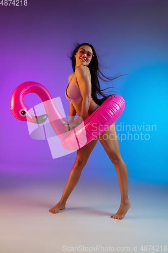 Image of Fashion portrait of young fit and sportive woman in purple luxury swimwear and stylish sunglasses on gradient background. Perfect body ready for summertime.