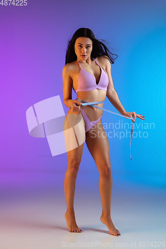 Image of Fashion portrait of young fit and sportive woman in purple luxury swimwear on gradient background. Perfect body ready for summertime.