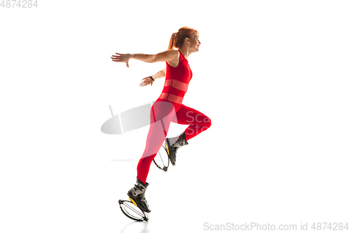 Image of Beautiful redhead woman in a red sportswear jumping in a kangoo jumps shoes isolated on white studio background.