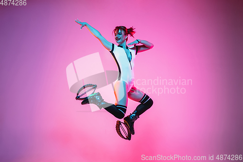 Image of Beautiful redhead woman in a white sportswear jumping in a kangoo jumps shoes isolated on gradient studio background in neon light