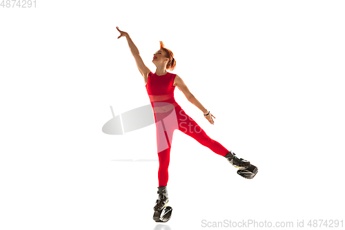 Image of Beautiful redhead woman in a red sportswear jumping in a kangoo jumps shoes isolated on white studio background.