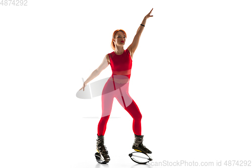 Image of Beautiful redhead woman in a red sportswear jumping in a kangoo jumps shoes isolated on white studio background.