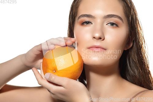 Image of Close up of beautiful female face with orange over white background. Cosmetics and makeup, natural and eco treatment, skin care.