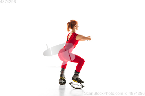 Image of Beautiful redhead woman in a red sportswear jumping in a kangoo jumps shoes isolated on white studio background.