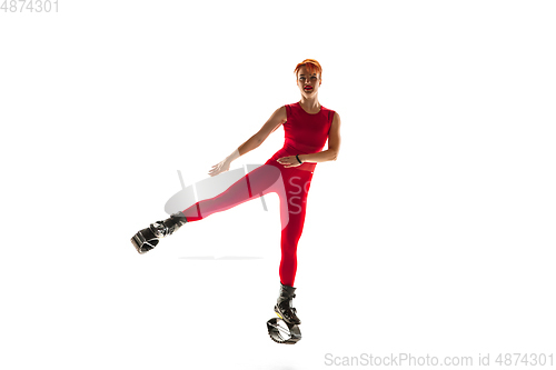 Image of Beautiful redhead woman in a red sportswear jumping in a kangoo jumps shoes isolated on white studio background.