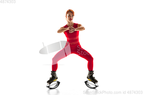 Image of Beautiful redhead woman in a red sportswear jumping in a kangoo jumps shoes isolated on white studio background.