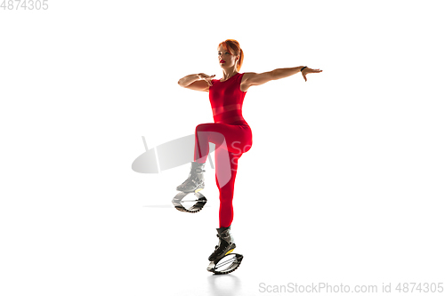 Image of Beautiful redhead woman in a red sportswear jumping in a kangoo jumps shoes isolated on white studio background.