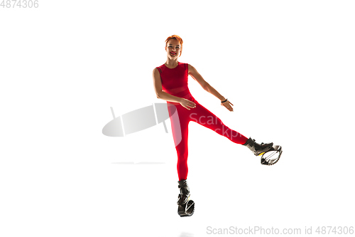 Image of Beautiful redhead woman in a red sportswear jumping in a kangoo jumps shoes isolated on white studio background.