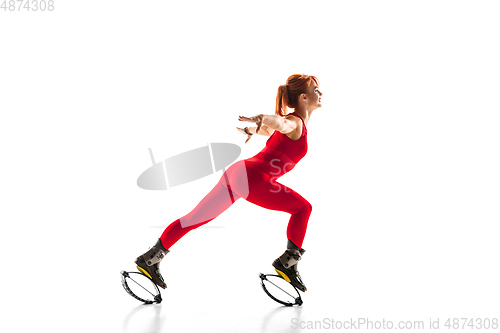 Image of Beautiful redhead woman in a red sportswear jumping in a kangoo jumps shoes isolated on white studio background.