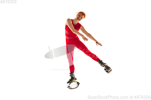 Image of Beautiful redhead woman in a red sportswear jumping in a kangoo jumps shoes isolated on white studio background.