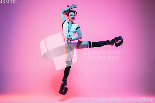 Image of Beautiful redhead woman in a white sportswear jumping in a kangoo jumps shoes isolated on gradient studio background in neon light