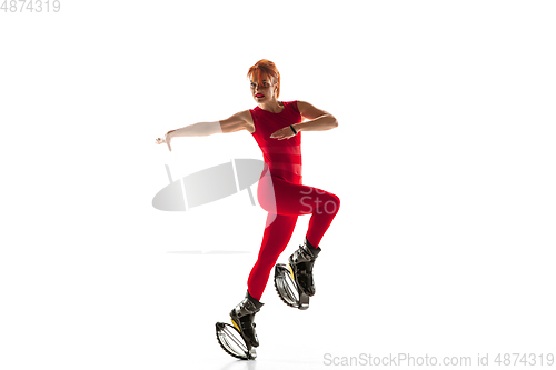 Image of Beautiful redhead woman in a red sportswear jumping in a kangoo jumps shoes isolated on white studio background.