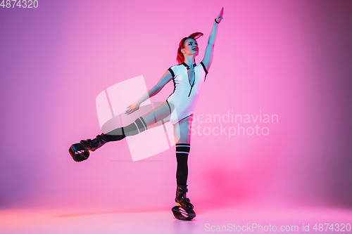 Image of Beautiful redhead woman in a white sportswear jumping in a kangoo jumps shoes isolated on gradient studio background in neon light