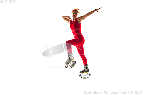 Image of Beautiful redhead woman in a red sportswear jumping in a kangoo jumps shoes isolated on white studio background.