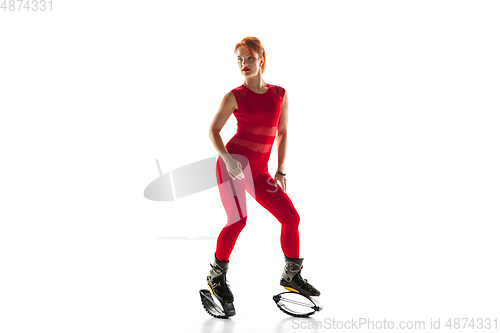Image of Beautiful redhead woman in a red sportswear jumping in a kangoo jumps shoes isolated on white studio background.
