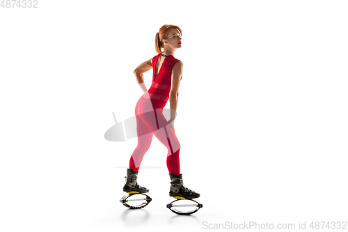 Image of Beautiful redhead woman in a red sportswear jumping in a kangoo jumps shoes isolated on white studio background.
