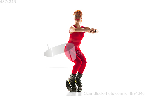 Image of Beautiful redhead woman in a red sportswear jumping in a kangoo jumps shoes isolated on white studio background.