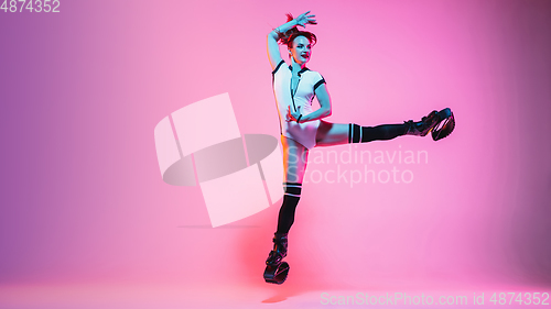 Image of Beautiful redhead woman in a white sportswear jumping in a kangoo jumps shoes isolated on gradient studio background in neon light